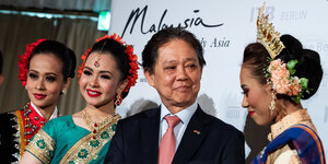 Drei Frauen und ein Mann vor einem Schild mit Aufschirft "Malaysia"