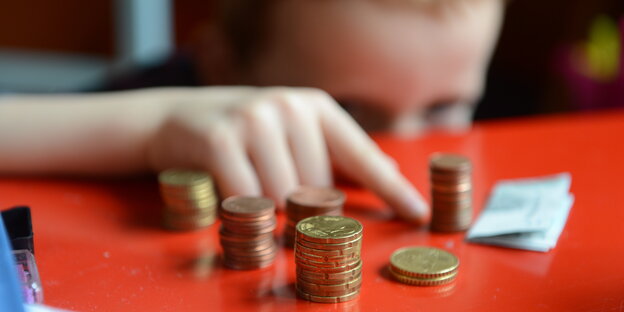 Auf einem Tisch liegen Centstücke, ein Kind zeigt darauf