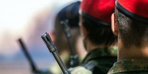 Neben einem uniformierten Bundeswehrsoldaten ist der Mündungslauf einer Waffe zu sehen