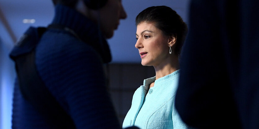 Sahra Wagenknecht, die Fraktionsvorsitzende der Partei Die Linke, steht zweien zwei Menschen im Licht