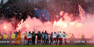 Die Spiler des HSV lassen sich von Fans mit bengalischen Feuern feiern.