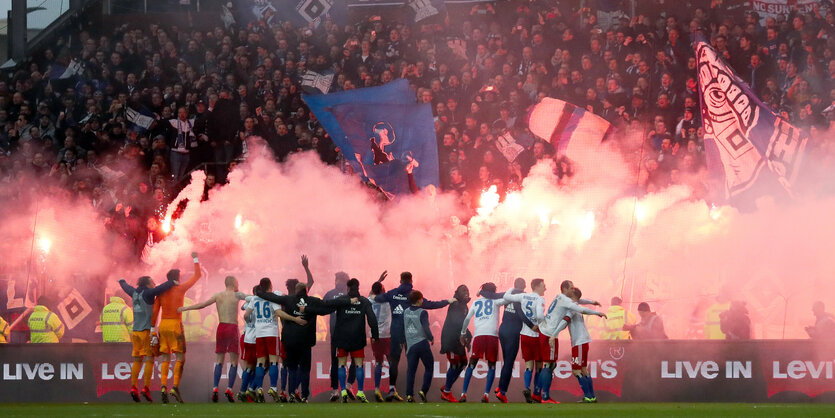 Die Spiler des HSV lassen sich von Fans mit bengalischen Feuern feiern.