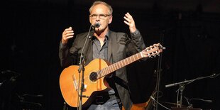 Reinhold Beckmann gestikulierend mit Gitarre auf einer Bühne