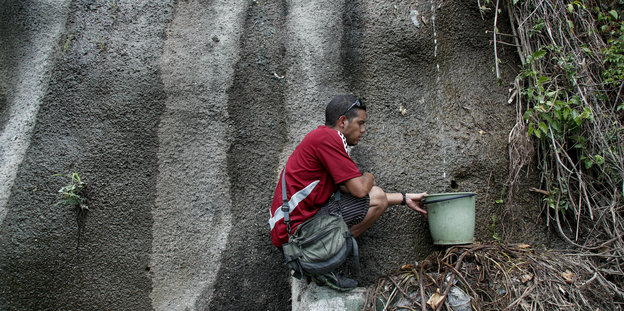 Ein Mann sammelt Wasser an einer Felswand