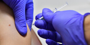 Eine Person wird in mit einer Impfspritze in den Arm gestochen