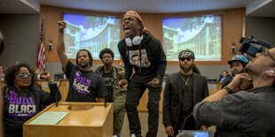 Demonstrant*innen im Stadtrat von Sacramento. Ein Mann schreit, zwei andere Personen recken die Faust in die Höhe