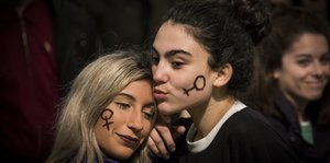 Zwei Frauen halten ihren Kopf aneinander, beide haben das sogenannte Venussymbol auf das Gesicht gemalt