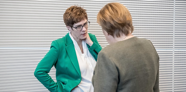 Annegret Kramp-Karrenbauer steht Angela Merkel gegenüber und spricht mit ihr