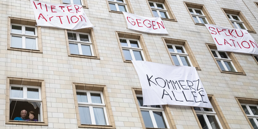 Ein älteres Pärchen schaut aus dem Fenster in der Karl-Marx-Allee. Es hängen Transparente