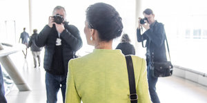 Sahra Wagenknecht mit dem Rücken zur Kamera läuft einen Gang hinunter und wird von der Presse fotografiert.