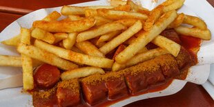 Eine Currywurst mit Pommes frites liegt in einer Schale