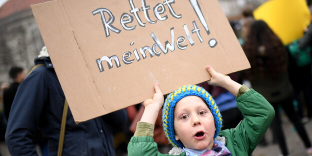 Ein kleiner Junge hält ein Schild mit der Aufschrift: „Rettet meine Welt“