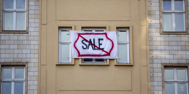 Aus dem Fenster einer Wohnung hängt ein Banner mit der Aufschrift "Sale". Das Wort ist durchgestrichen