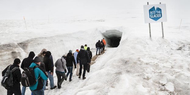 Eine Besuchergruppe geht in einer Schneelandschaft auf den Eingang eines Tunnels zu