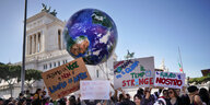 Viele junge Menschen auf einem Platz in Rom halten Transparente, Plakate und eine aufgepustete Weltkugel hoch
