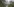 Schotterpiste durch eine grüne Landschaft, im Hindergrund hohe, teilweise mit Schnee bedeckte Berge zu sehen
