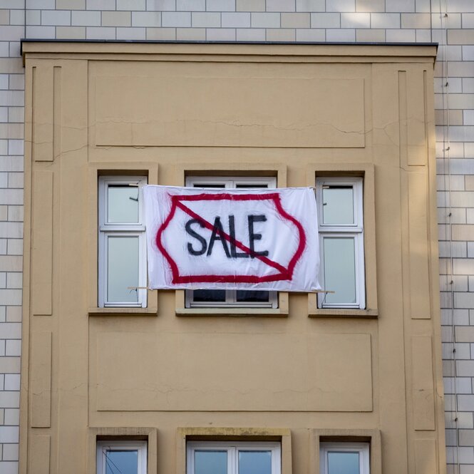 Transparent mit dem durchgestrichenen Wort SALE an einer Gebäudefassade in der Karl-Marx-Allee