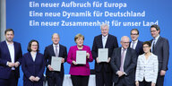 Mehrere Menschen, darunter Angela Merkel, Andrea Nahles und Horst Seehofer stehen vor einer blauen Wand