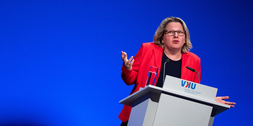 Svenja Schulze steht im roten Blazer auf einem Podium hinter einem Pult und redet