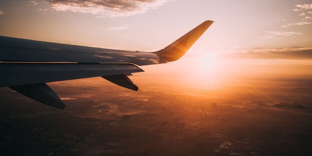 Die Tragfläche eines Flugzeugs, dahinter die aufgehende Sonne