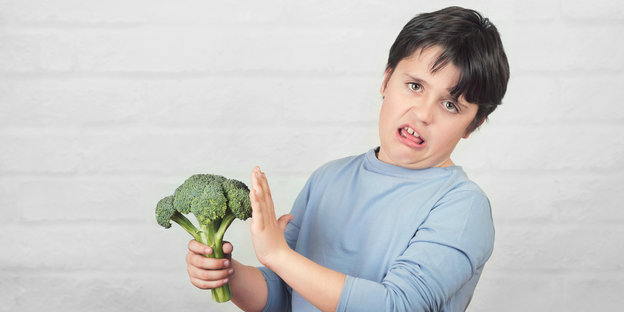 Ein Junge hält einen Brokkoli und schaut angewidert