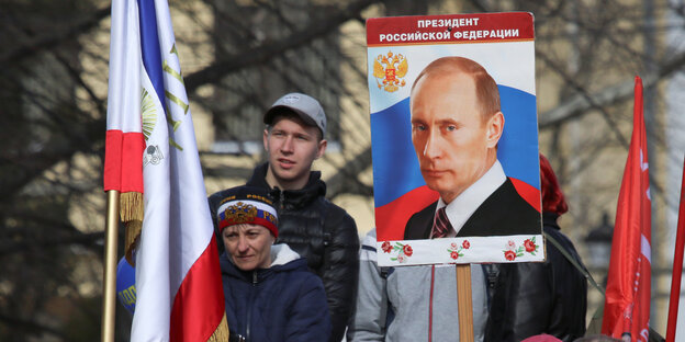Bei der Feier zur Annektierung der Krim trägt ein Mann ein Plakat mit einem Foto von Putin