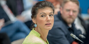 Sahra Wagenknecht sitzt vor einem Mikro inmitten mehrere Menschen