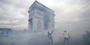 Der Pariser Triuphbogen ist von Rauch umgeben, zwei Männer stehen davor. Ein Mann trägt eine gelbe Weste