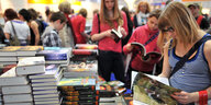 Jugendliche Mädchen stehen auf der Buchmesse vor Bücherstapeln und lesen jeweils in einem Buch