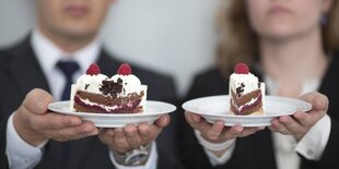 Ein Mann und eine Frau halten ein Stück Torte. Der Mann hat der größere Stück vom Kuchen