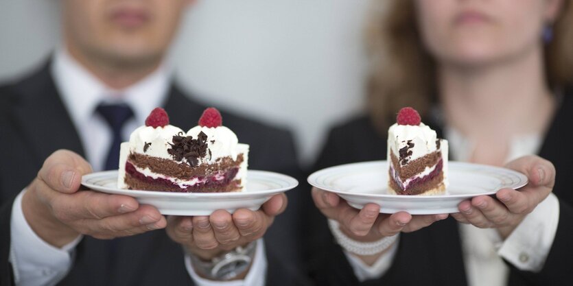 Ein Mann und eine Frau halten ein Stück Torte. Der Mann hat der größere Stück vom Kuchen