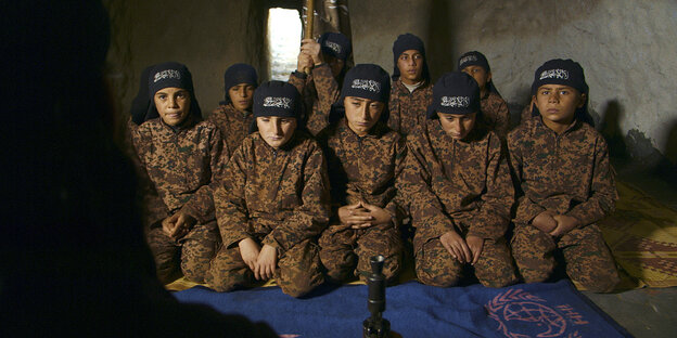 Jungs in Militärkleidung sitzen in einem dunklen Raum vor einer Wasserpfeife