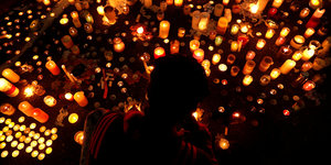 Ein Mensch steht vor vielen Kerzen, die um die Opfer von Christchurch gedenken