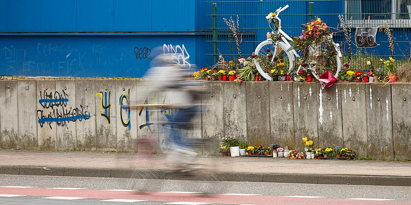 Weißes Fahrad steht mit Blumen geschmückt auf einer Mauer