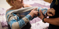 Eine Pflegekraft hilft einer alten Frau beim Ausziehen eines Pullovers.