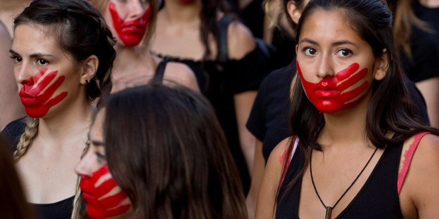 Mehrere Frauen bei einer Demonstration, sie haben rote Farbe im Gesicht, die die Form einer Hand hat