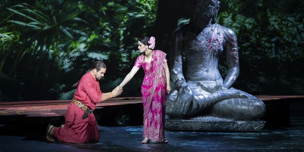 Vor einer Buddhastatue kniet ein Mann von einer Frau, beide in Saris