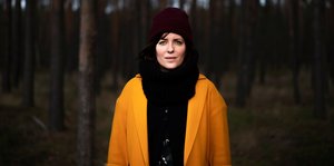 Sarah Kuttner mit Mütze und in gelber Jacke in einem Wald