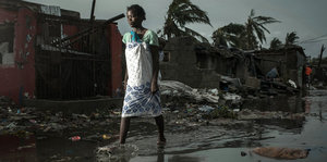 Eine Frau geht eine überflutete Straße entlang, zerstörte Häuser