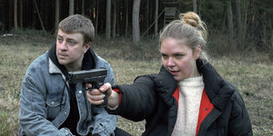 Ein junger Mann und eine junge Frau, sie zielt mit einer Waffe auf etwas