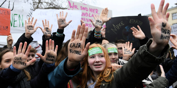 Jugendlich auf einer Klimademo, sie strecken die Innenhand nach vorn, auf ihnen steht: "Our Future" und "In your hands"