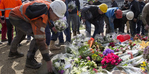 Menschen mit Signalwesten und Schutzhelmen legen Blumen auf den Boden.