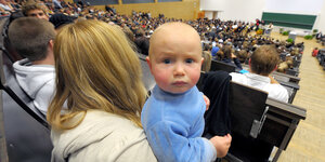 Eine Frau sitzt mit einem Baby auf dem Arm in einem Hörsaal.