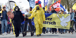 Menschen sind teilweise verkleidet und gehen gemeinsam mit Transparenten und Plakaten auf die Kamera zu