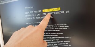 Ein Finger zeigt auf einen Bildschirm, auf dem die schwarze Wikipedia-Seite zu sehen ist. Die Wörter "Letzte Chance" sind gelb hinterlegt