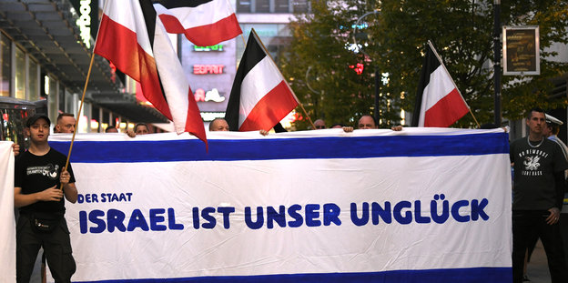 Demonstranten zeigen schwarz-weiß-rote Fahnen und ein Transparent mit der Aufschrift "Der Staat Israel ist unser Unglück"