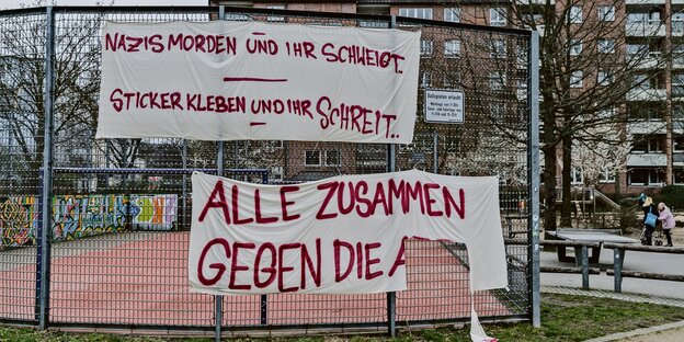 An einem Sportplatz-Zaun hängt ein Plakat mit der Aufschrift "Nazis morden und ihr schweigt - Sticker kleben und ihr schreit".