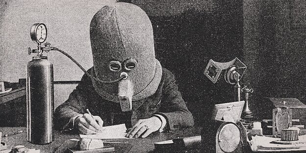 Ein Mensch mit einer Maske sitzt an einem Schreibtisch.