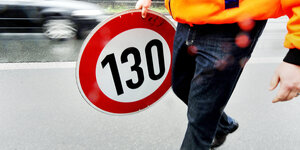 Eine Person trägt ein Verkehrsschild, das 130 km pro Stunde als Höchstgeschwindigkeit vorschreibt