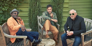 drei Männer sitzen auf Holzstühlen nebeneinander